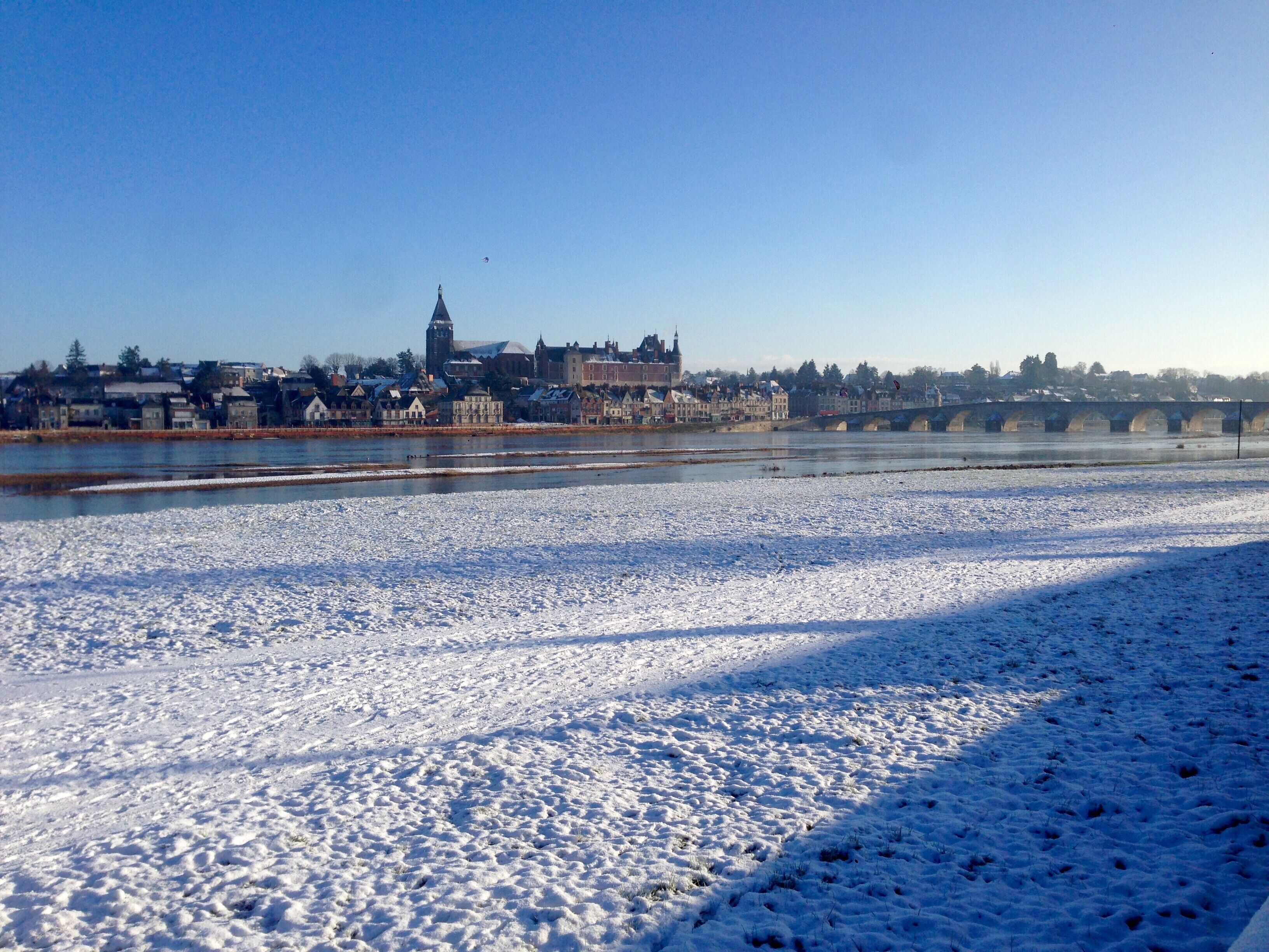 Een met sneeuw bedekte oever met een brug en historische gebouwen op de achtergrond.