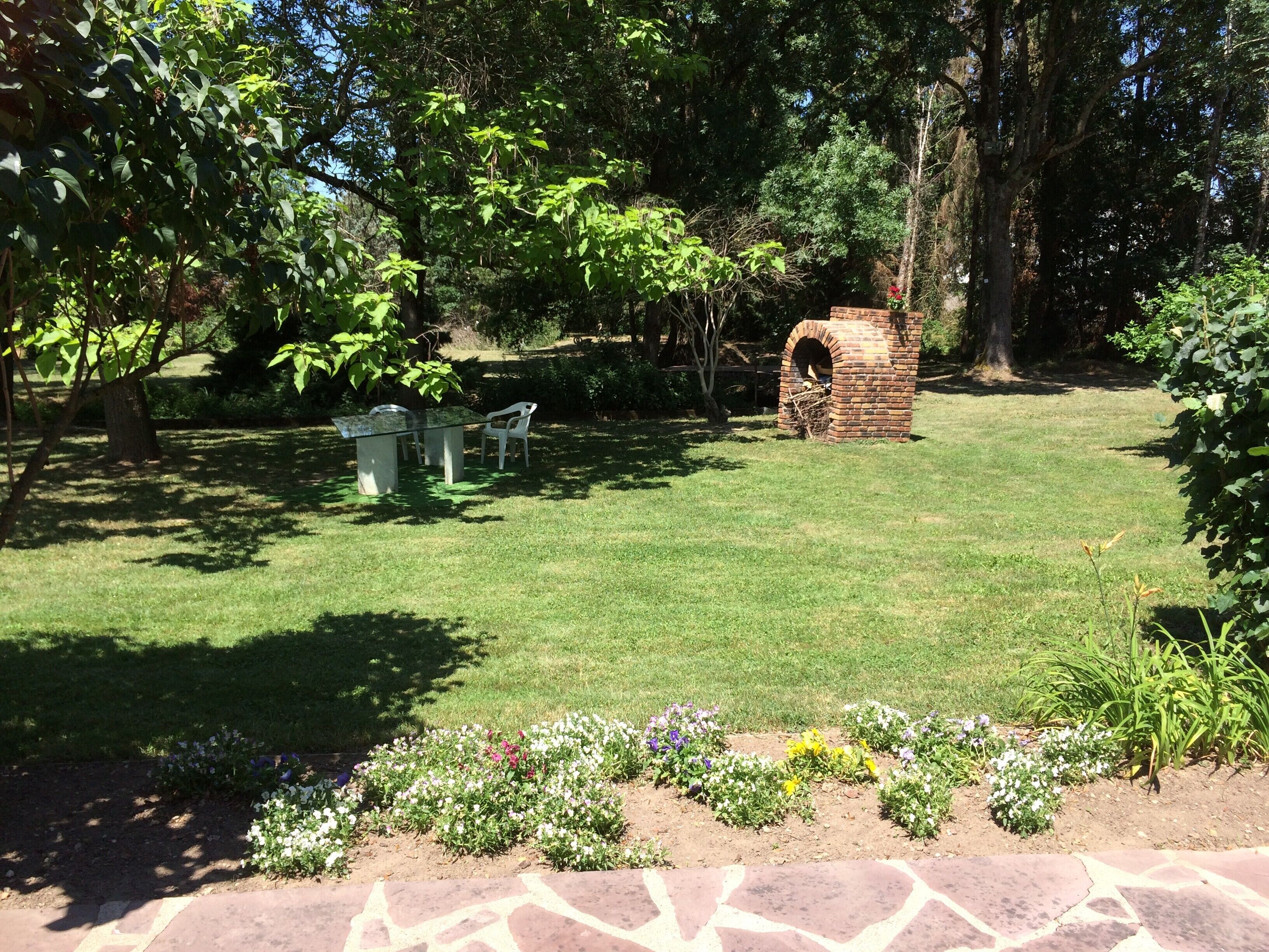 Un jardí amb una zona de barbacoa de maó, un camí de pedra i una taula amb cadires.