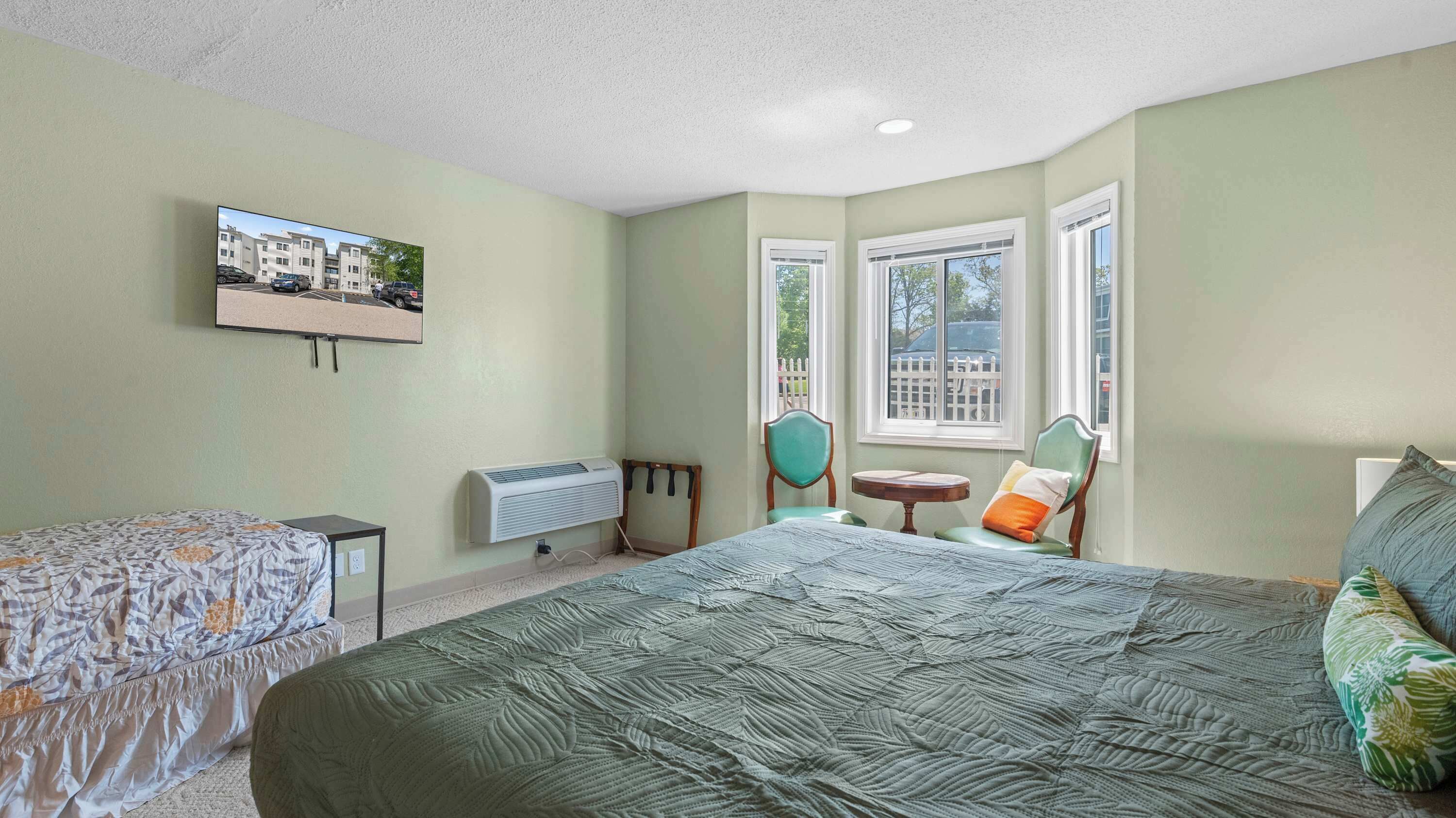 A bedroom with a bed, a chair, a small table, a heater, and a TV mounted on the wall.