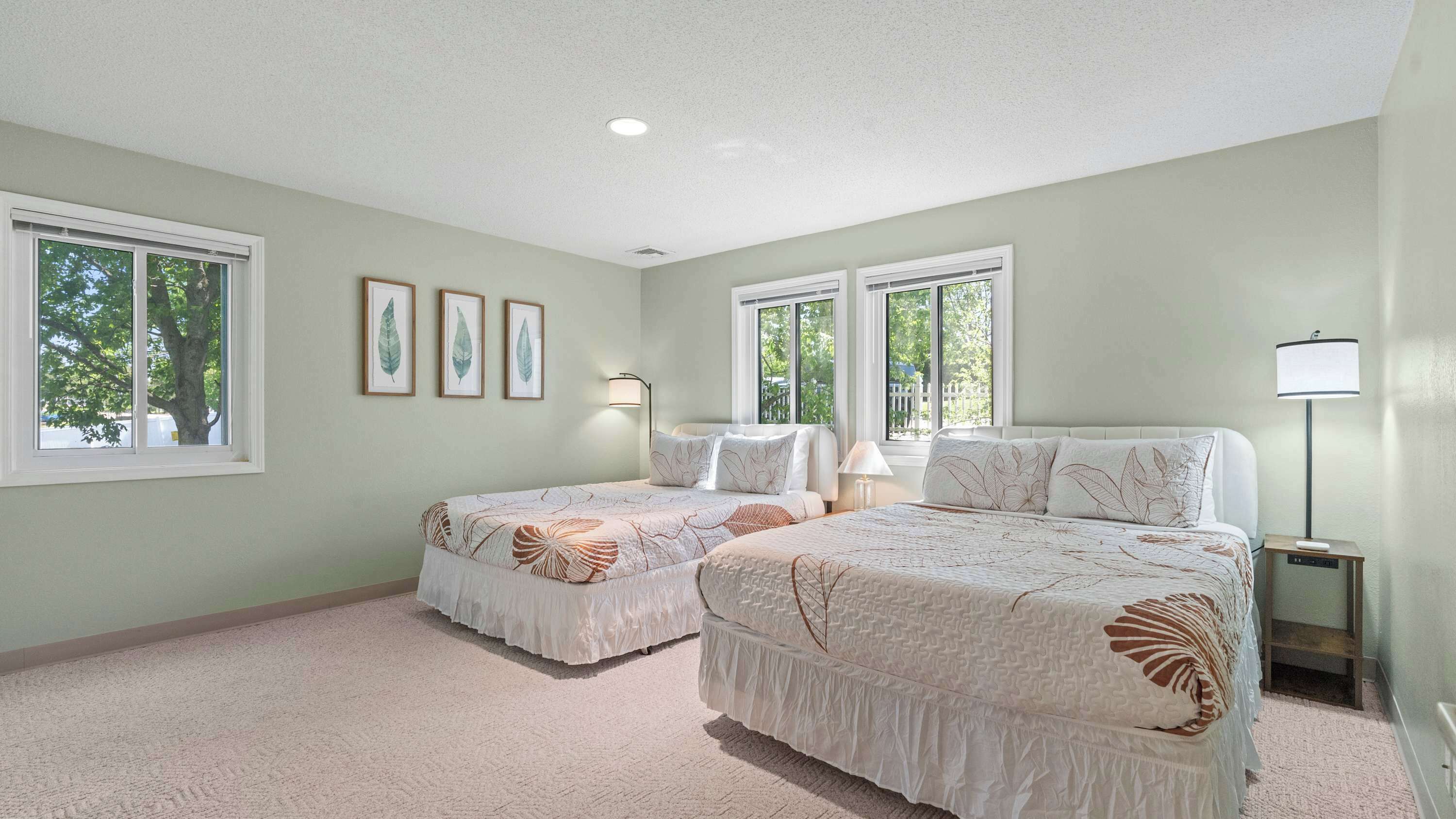 A bedroom with two beds, a nightstand, a lamp, and framed leaf artwork on the wall.