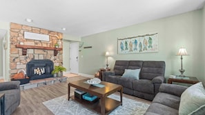 A living room with a stone fireplace, a sofa, a coffee table, and a painting of fish on the wall. - Have It All Stay Central, Swim Often (Osage Beach)