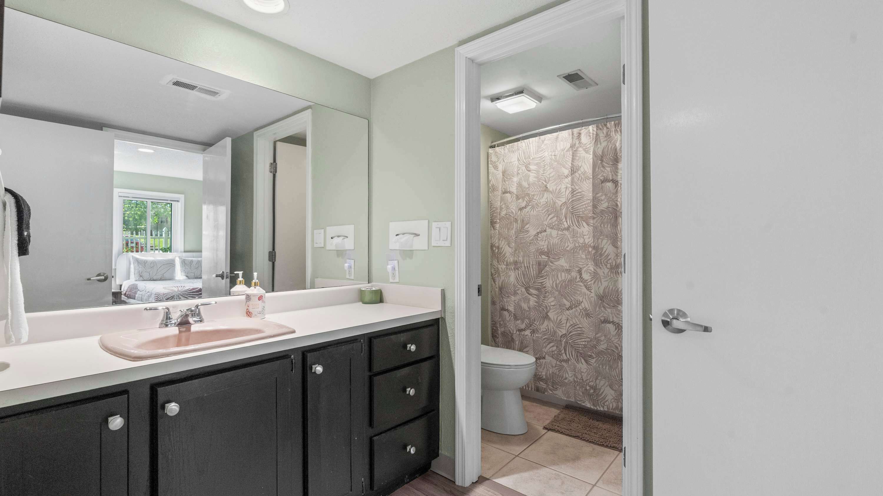 Un bagno con uno specchio grande, un lavandino con rubinetto, un water e una tenda da doccia.