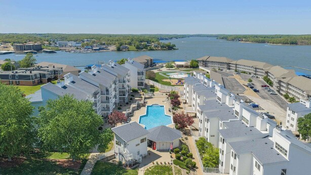 A waterfront hotel with multiple-story buildings, a central swimming pool, and a marina in the background. - Have It All Stay Central, Swim Often (Osage Beach)