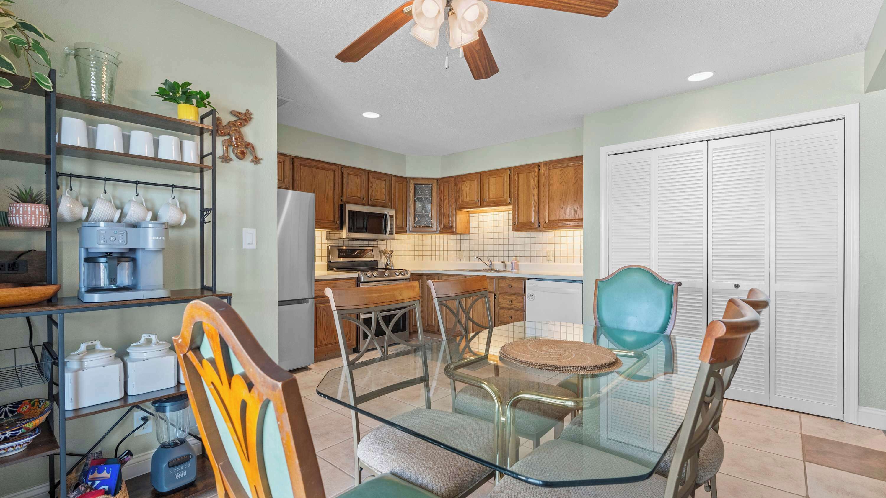 A kitchen with wooden cabinets, a refrigerator, a coffee maker, and a dining area with a glass table and chairs.
