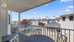 A balcony with a view of a swimming pool, adjacent buildings, and a covered outdoor seating area. - Have It All Stay Central, Swim Often (Osage Beach)