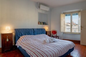 A bedroom with a bed, bedside lamps, a bookshelf, a window, and an air conditioning unit. - Holiday Home "Le tre finestre sull'Anfiteatro - Lucca" with Wi-Fi and Air Conditioning (Lucca)