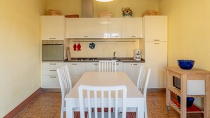 Een kleine keuken met witte kastjes, een eettafel met stoelen, een fornuis en een spoelbak.