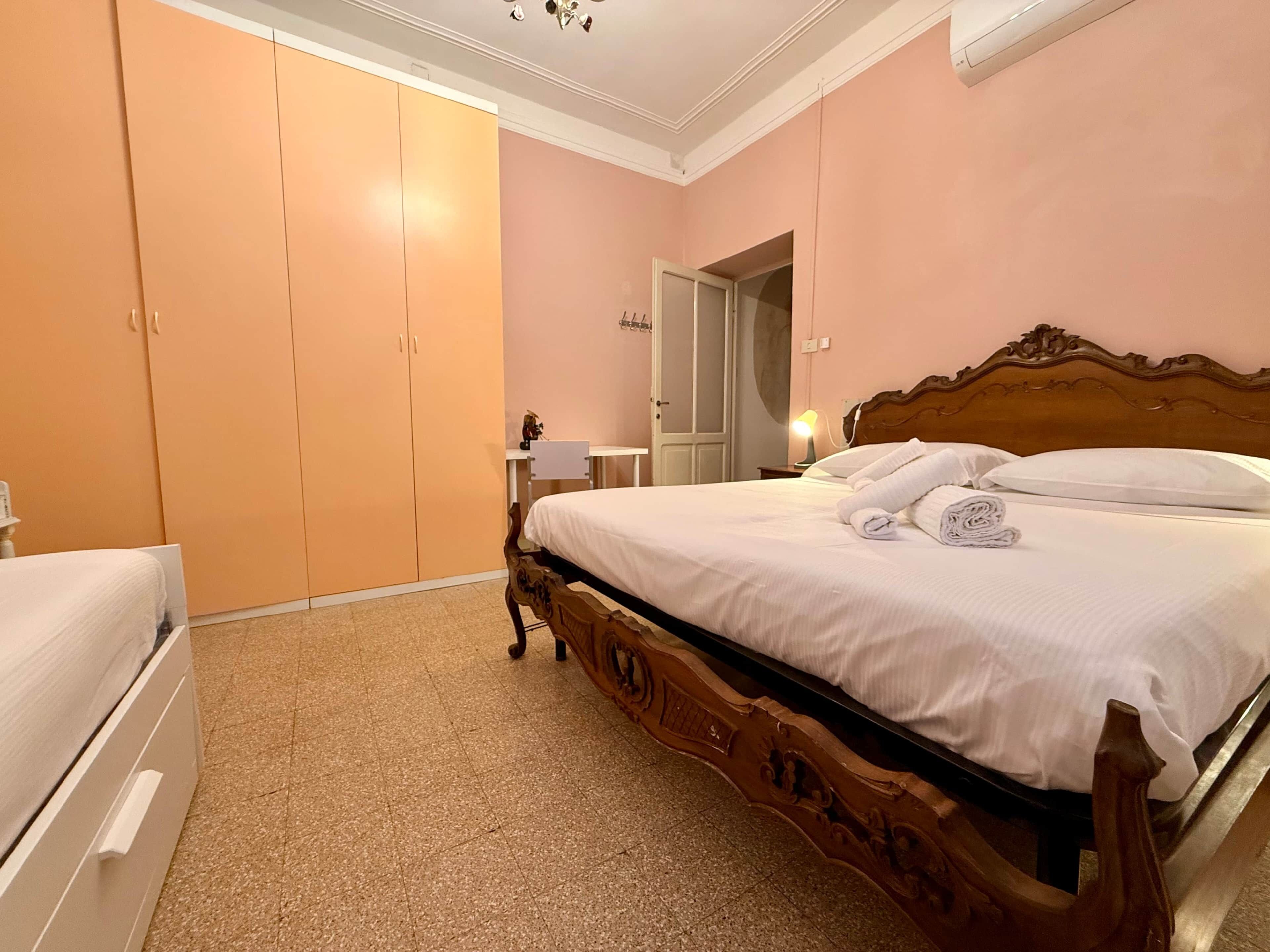 Un dormitorio con cama de madera, un armario, un escritorio y una puerta que da a otra habitación.