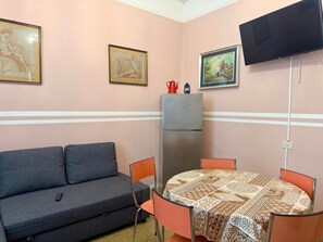 A room with a sofa, a table with chairs, a refrigerator, and wall-mounted artwork. - La Gardenia /of the Duchy (Parma)