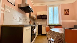 Una cocina compacta con una isla central, un comedor con mantel estampado y un ventanal con cortinas.
