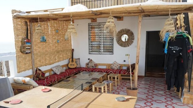 A cozy outdoor seating area with a wooden bench, a glass table, and a hanging guitar. - Epicswellhouse (Aourir)