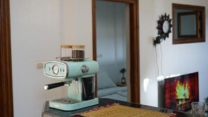 A retro-style espresso machine on a table with a woven placemat. A television displaying a fire image is in the background. - Epicswellhouse (Aourir)