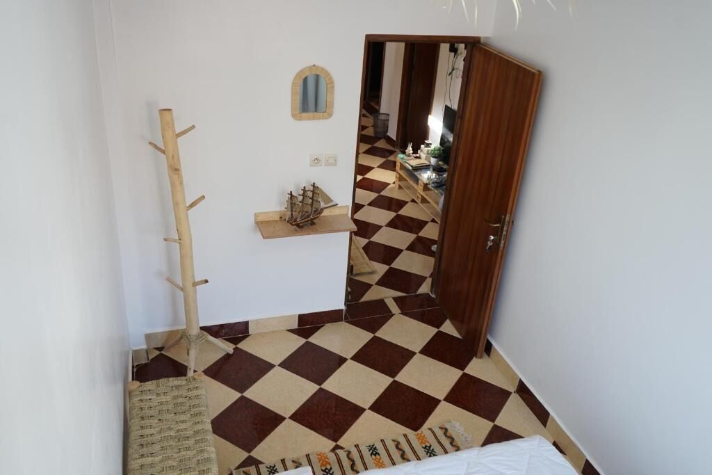 A room with a checkered floor, a coat rack, a small shelf with a ship model, and a mirror on the wall.