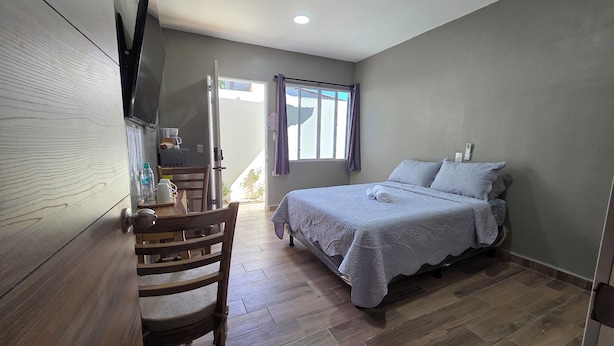 A bedroom with a bed, a desk with a chair, a window, and a door leading outside.