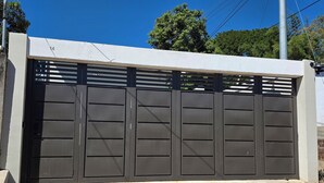 A gated entrance with a stone-paved driveway leading up to a white wall.