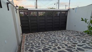 A courtyard with a stone floor, a metal gate, and a white wall.