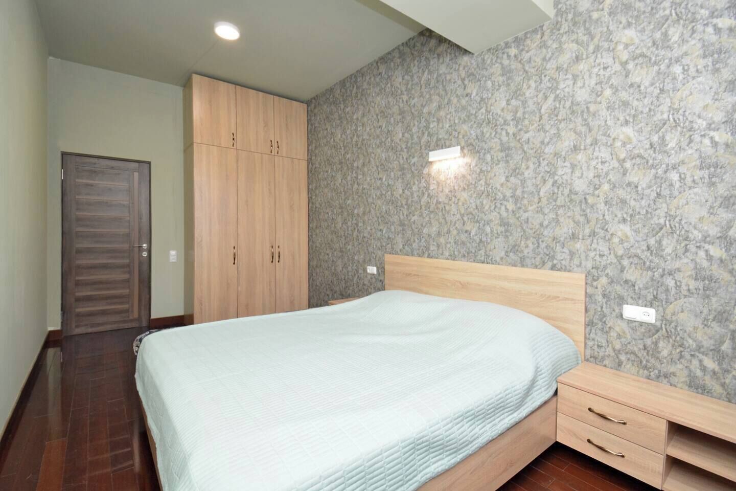 A bedroom with a bed, wooden wardrobe, and a marble-patterned wall.