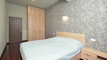 A bedroom with a bed, wooden wardrobe, and a marble-patterned wall.