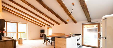 A modern kitchen with wooden beams, a dining area, and a view to the outside.