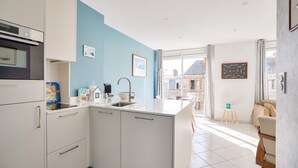 Eine moderne Küche mit weißen Schränken, einer blauen Akzentwand und einem großen Fenster.