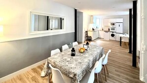 Un espace repas moderne avec une nappe à motifs, des chaises blanches et un saladier rempli de fruits.