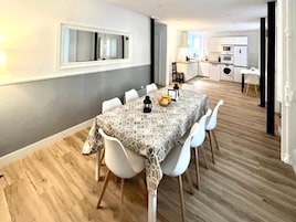 Un comedor moderno con un mantel estampado, sillas blancas y un frutero.