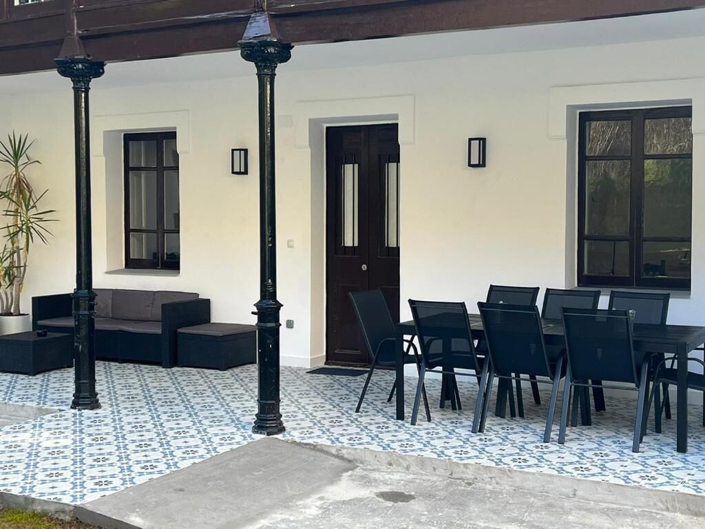 An outdoor seating area with a tiled floor, a sofa, a table with chairs, and two black lampposts.
