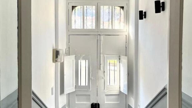 Un couloir avec une porte à deux battants, une petite fenêtre et un interrupteur sur le mur.