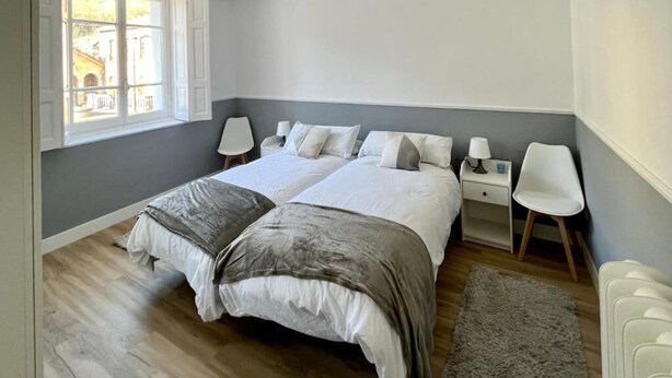 Un dormitorio con dos camas, una ventana, una mesita de noche, una silla y un radiador.