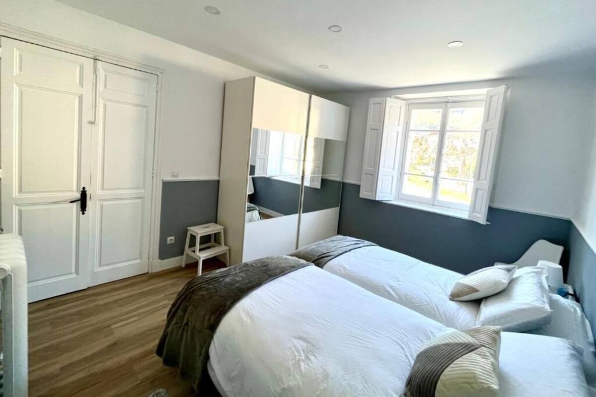 Een slaapkamer met twee bedden, een kledingkast, een klein krukje en een raam.