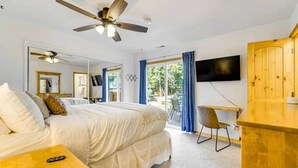 Quarto com cama, televisão, escrivaninha e ventoinha no teto.
