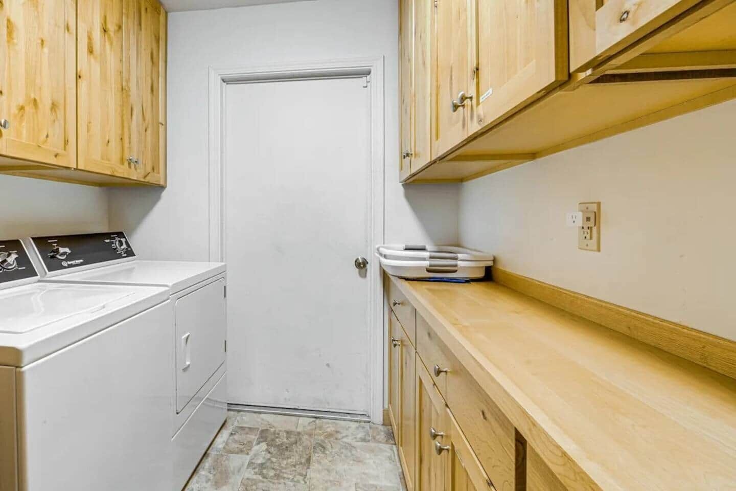 A laundry room with a washing machine, a dryer, wooden cabinets, and a scale on the counter.