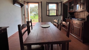 Un coin repas avec une table et des chaises en bois, une fenêtre avec des rideaux et un espace cuisine comprenant des placards et un évier.