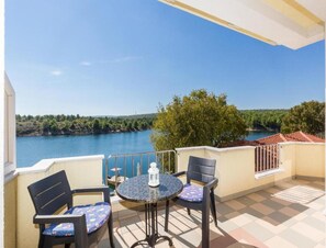 A balcony with a table and two chairs, overlooking a body of water and greenery. - Pool View Apartment With Balcony in Obrovac (Obrovac)