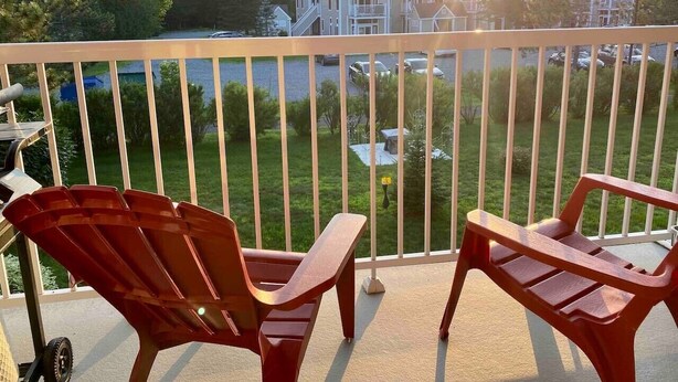 Een balkon met twee houten stoelen en uitzicht op een woonwijk, onder een heldere lucht.