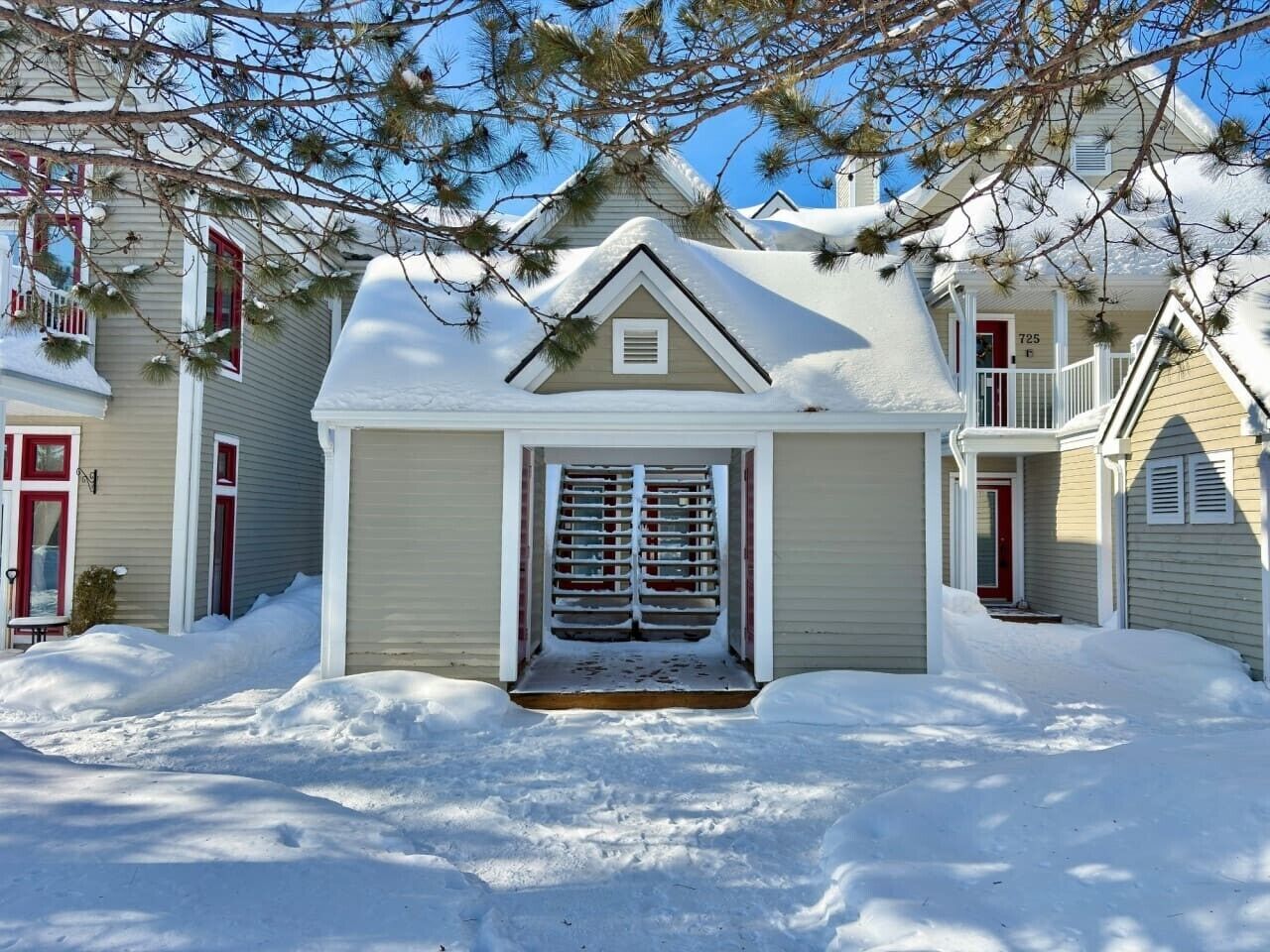 Une maison d’habitation dont l’entrée est recouverte de neige, avec un petit porche et une porte rouge.