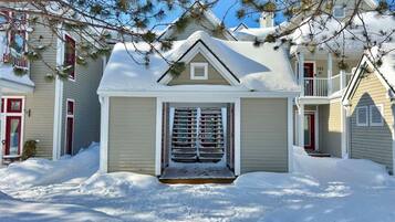 Une maison d’habitation dont l’entrée est recouverte de neige, avec un petit porche et une porte rouge.