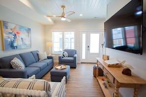 A living room with a sofa, armchair, ottoman, wooden coffee table, and a flat-screen TV.