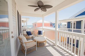 A covered porch with wicker furniture, a ceiling fan, and a view of colorful houses.