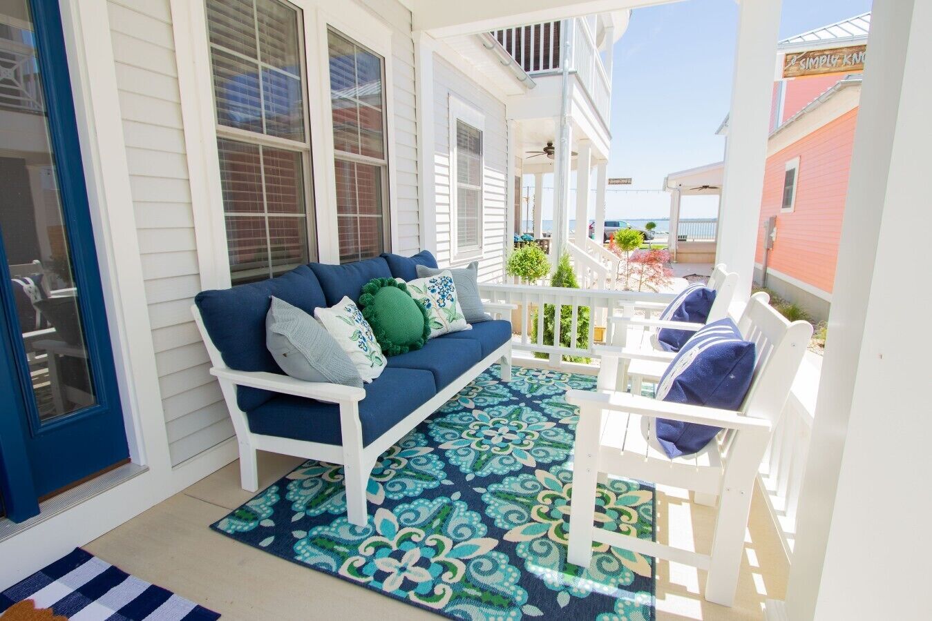 Un portico coperto con un divano blu, sedie bianche e un tappeto decorato.
