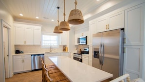 Una cocina moderna con armarios blancos, electrodomésticos de acero inoxidable, una isla grande y una zona de comedor de madera.