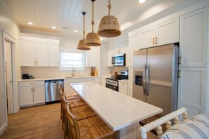 A modern kitchen with white cabinetry, stainless steel appliances, a large island, and a wooden dining area.