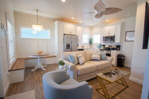 A modern kitchen with white cabinets, a dining area with a round table, a sofa, and a glass coffee table.