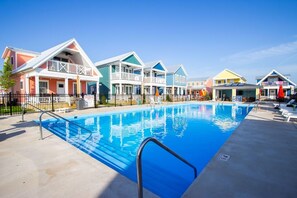 A swimming pool with a clear blue water surface, surrounded by colorful houses with balconies, and a black fence enclosing the area. - Flyer Cove: 4 Bed/3 Bath Cozy Lakeside Cottage! (Celina)
