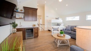 A modern living room with a kitchen, a bunk bed, and a grey sofa.