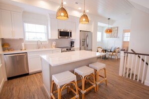 A modern kitchen with white cabinets, stainless steel appliances, and a large island with bar stools. - Flyer Cove: 4 Bed/3 Bath Cozy Lakeside Cottage! (Celina)