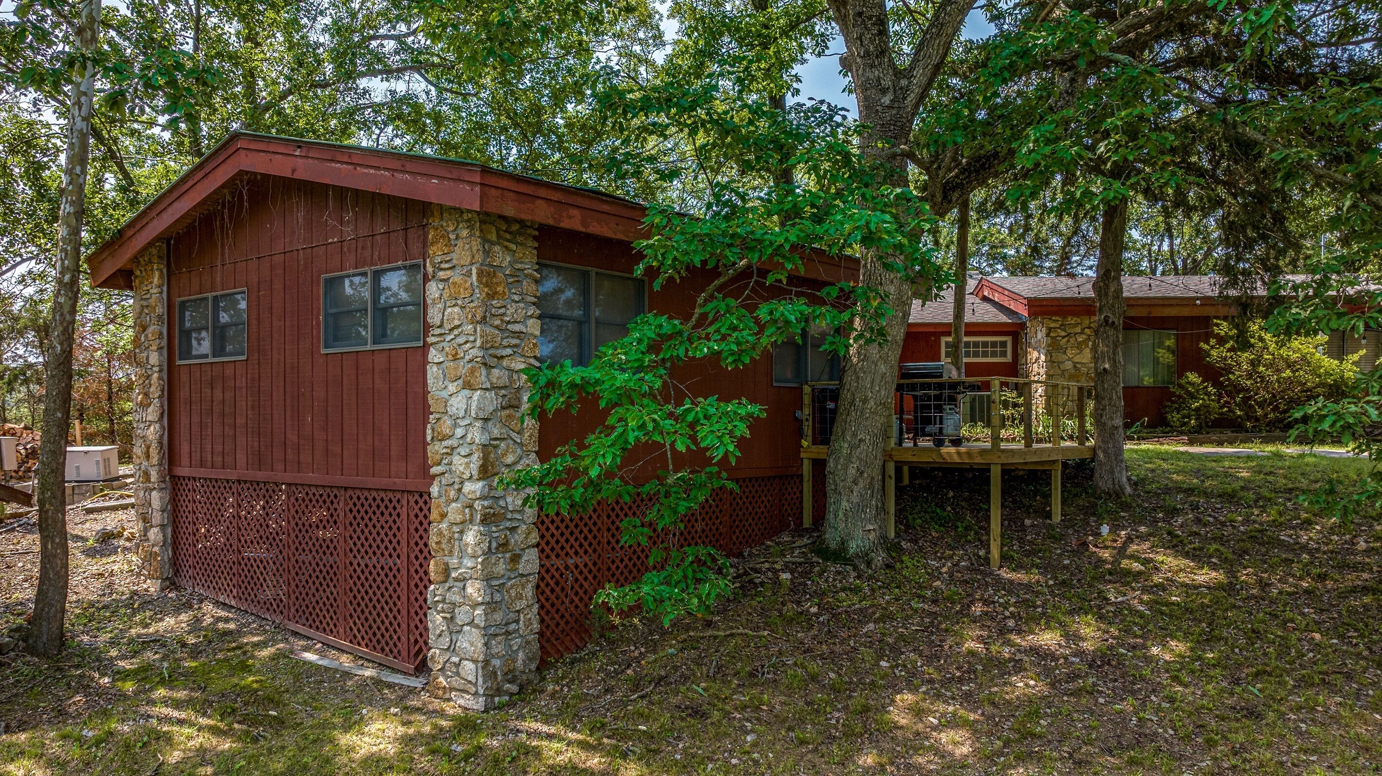 Une petite cabane avec des fondations en pierre et des murs en bois, entourée d’arbres et d’une zone herbeuse.