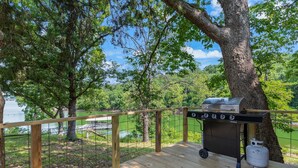 Une terrasse avec un barbecue et une bouteille de propane, offrant une vue sur un lac et une forêt.