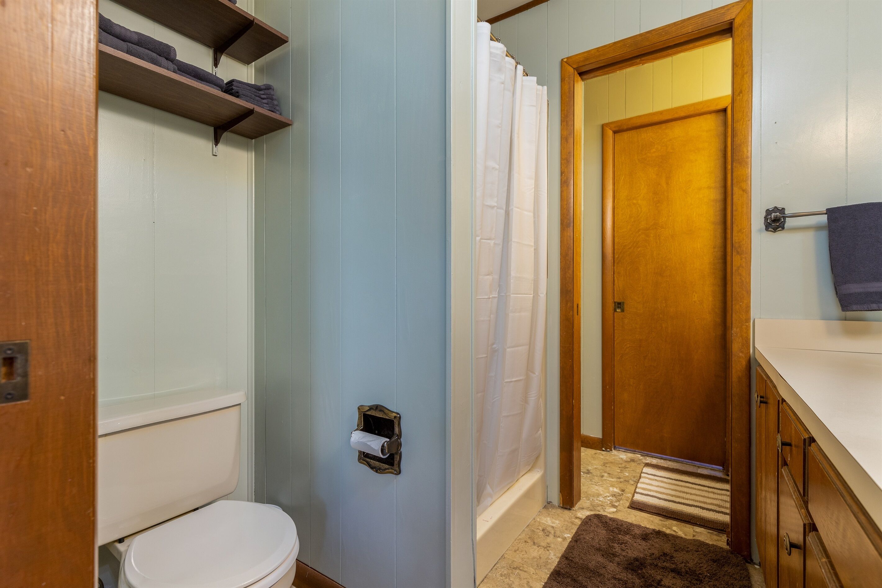 A bathroom with a toilet, a shower curtain, a wooden door, and a towel rack.