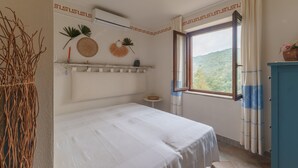 A bedroom with a bed, a window with curtains, a small table, and a decorative wall. - Vacation Home 'Villa Marisol Agrustos' with Private Terrace, Wi-Fi and Air Conditioning (Budoni)